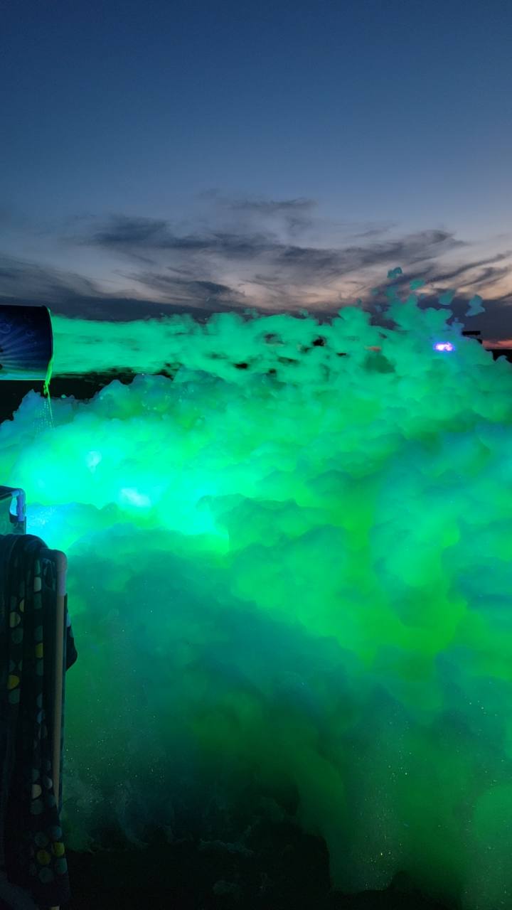 Green UV-reactive foam glowing beneath the evening sky at a Foamsational Fun party